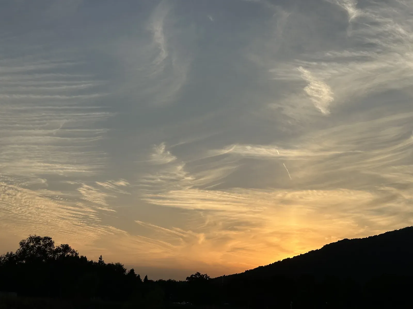Sunset at Jinwu Park: wispy clouds lit orange by the setting sun, above the silhouettes of a hill and trees